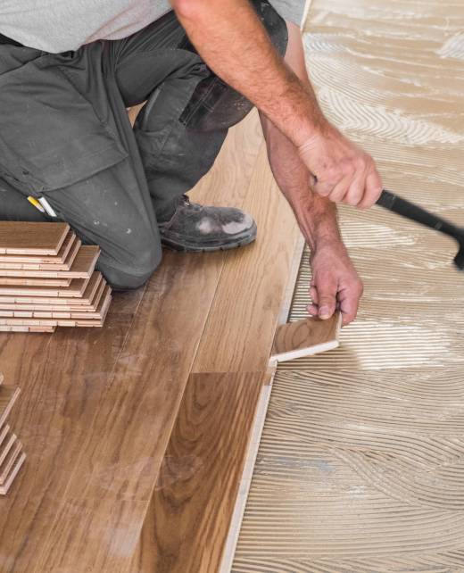 Worker installing wooden flooring boards on applied adhesive